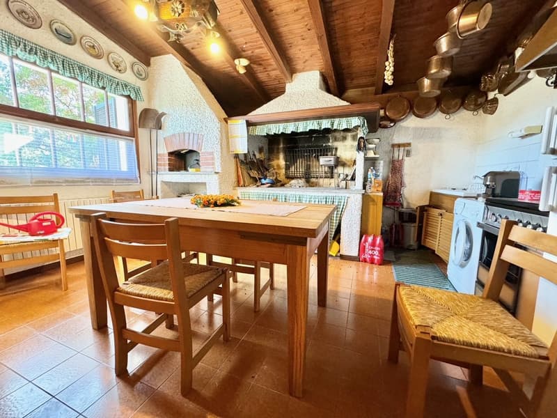 Rustic kitchen with wooden beamed ceiling, brick fireplace, wooden dining table and chairs, kitchen appliances and cookware on display