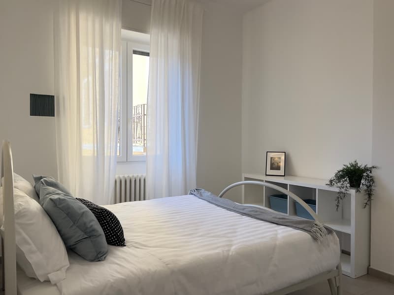 Double bed, white walls, white curtains, white shelves, bedside table, framed photo, plant