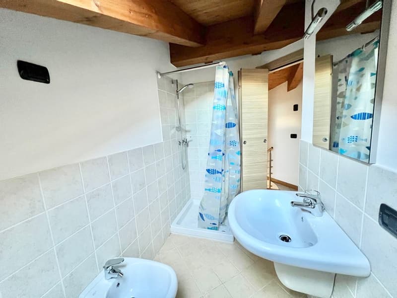 Tiled bathroom with shower stall, sink, and exposed wooden ceiling beams