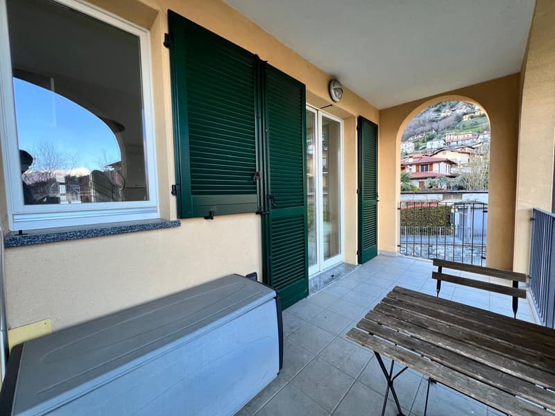 Spacious balcony with green shutters, tiled floor, wooden table and bench, large window with a view of the surrounding buildings and landscape