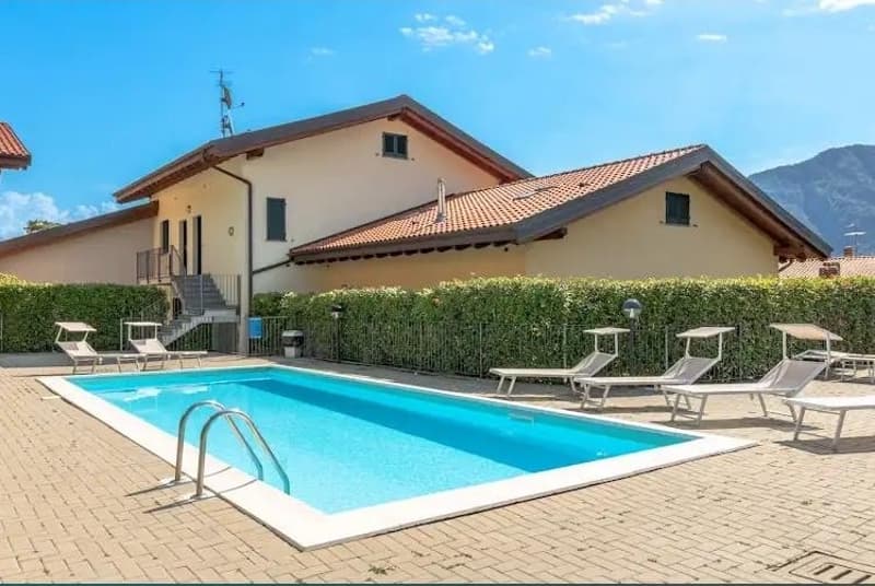Two-story house with red tile roof, surrounded by hedges, with a swimming pool and patio area in the front.