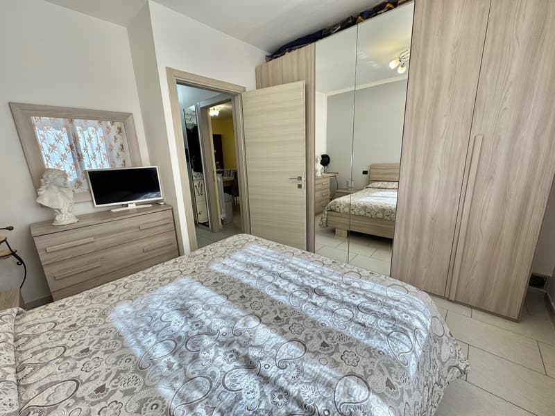 Bedroom with a bed, dresser, and a television. The room has a mirror and a large closet. The room is well-lit and has white walls and floors.