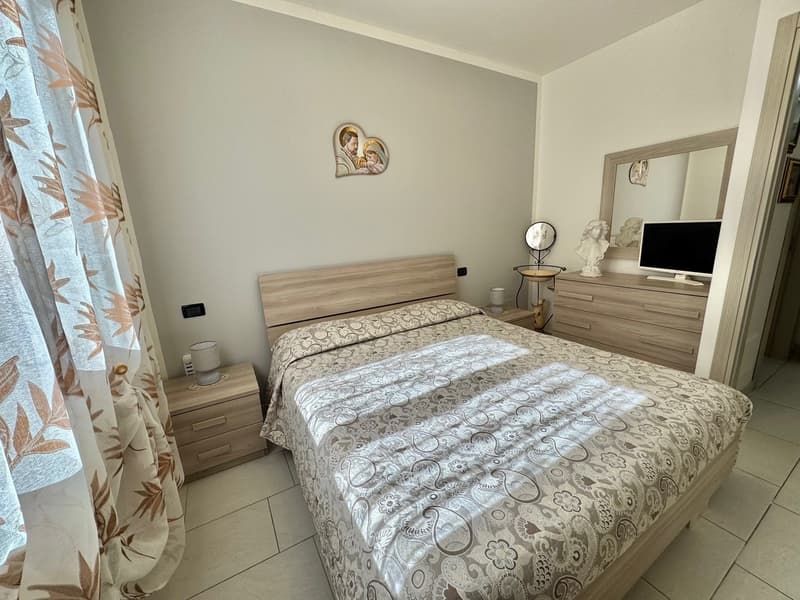 Bedroom with bed, nightstands, dresser, mirror, television, wall decor, curtains