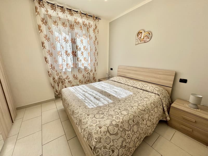 a bed with a patterned blanket, wooden nightstands with lamps, a picture frame on the wall, and curtains