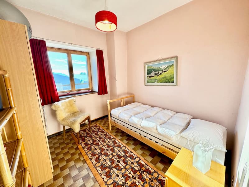 small room with bed, rug, chair, wooden cabinet, window with view