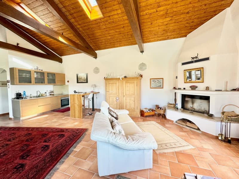 Spacious open-plan living area with wooden beamed ceiling, white walls, terracotta tile flooring, a fireplace, a sofa, and a kitchen area with wooden cabinets and appliances