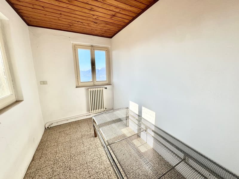 Small room with white walls, wooden ceiling, and a window with a view. The room has a tiled floor and a metal mesh structure, possibly used for storage or other purposes.