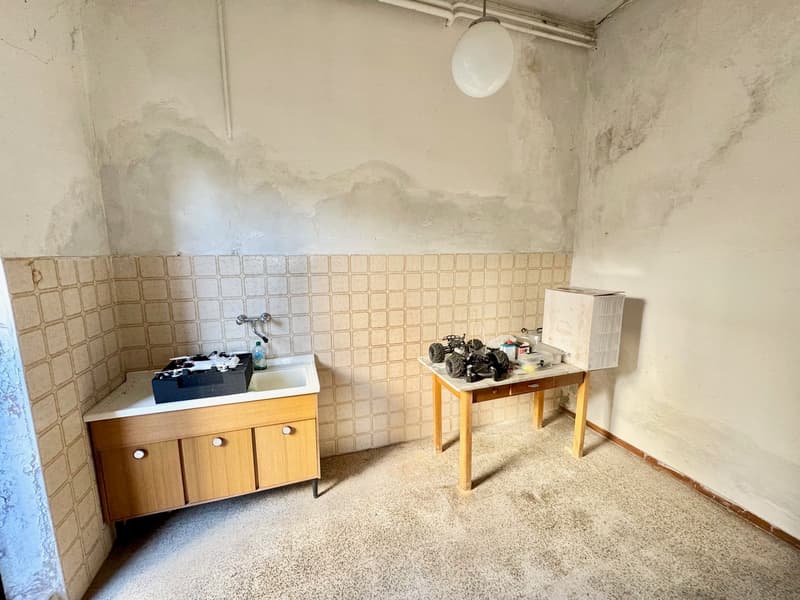 Utility room with tiled walls, wooden cabinet, and a table with various items on it.