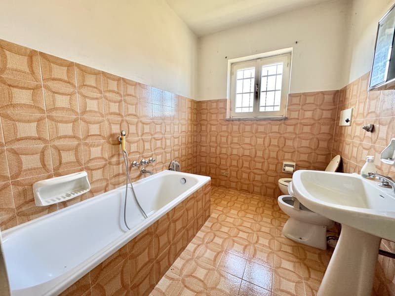 Bathroom with beige tiled walls and floor, a bathtub, a sink, and a toilet.