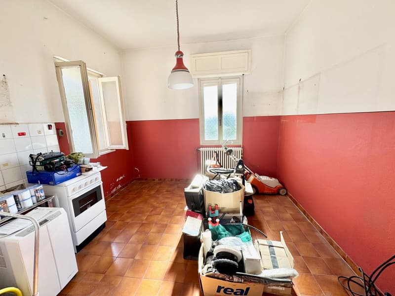 Cluttered kitchen with appliances, boxes, and a washing machine visible. The walls are painted in a red color scheme.