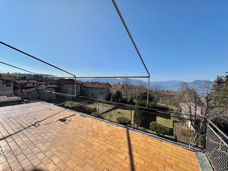 Large balcony with brick paving, metal railings, and a view of the surrounding buildings and mountains in the distance.