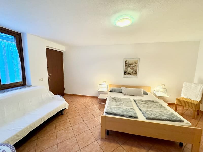 Spacious bedroom with tile flooring, white walls, large window, wooden bed frame, nightstands, and a framed artwork on the wall.
