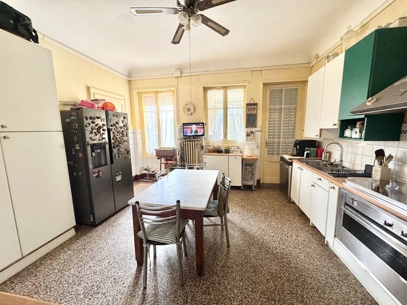 Spacious kitchen with white cabinets, tile flooring, dining table, ceiling fan, and various kitchen appliances including a refrigerator and dishwasher.