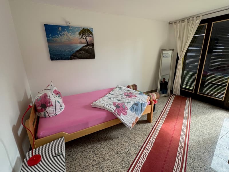a small bedroom with a single bed, a nightstand, a mirror, and a rug