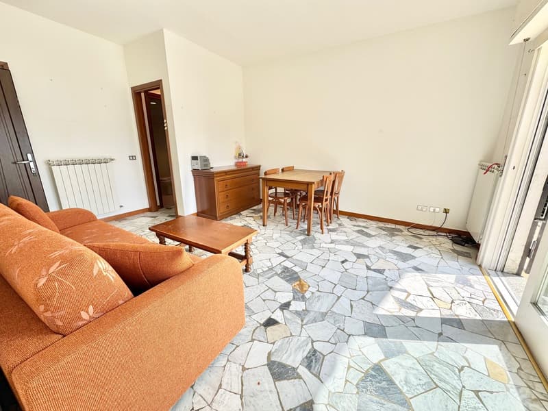 Living room with couch, coffee table, dining table, chairs, wooden cabinet, radiator, power outlets, sliding door