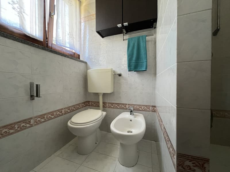 A small bathroom with toilet, bidet, window and towel rack.