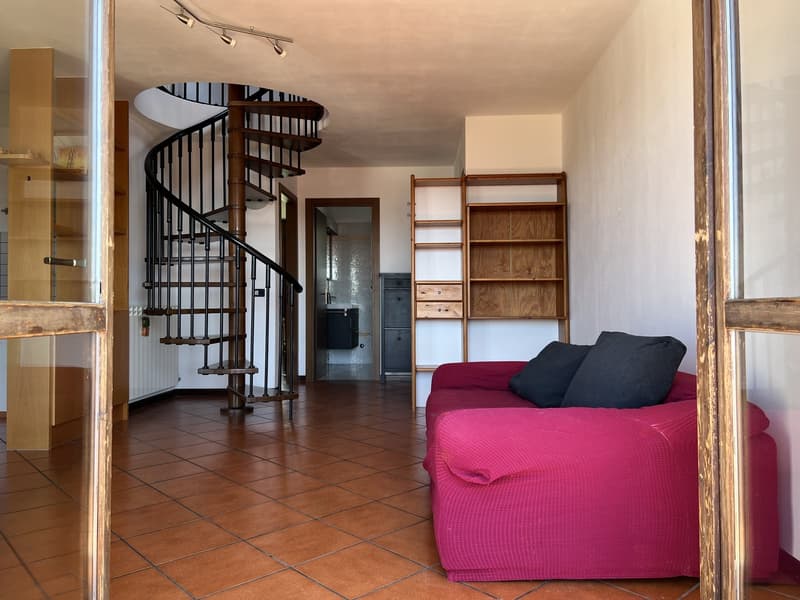 room with a spiral staircase, red couch, two black cushions, wooden shelves, radiator, tiled floor