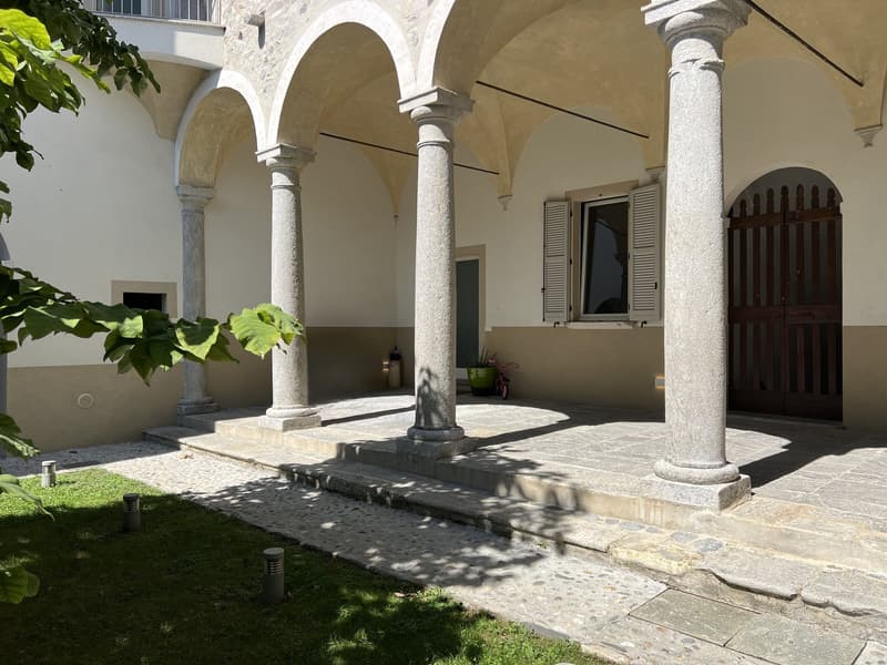 ample courtyard, classical style architecture, large stone pillars, small window, garden, wooden door