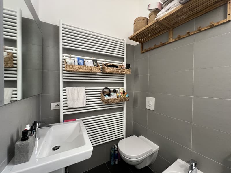 white sink, white toilet, wall-mounted radiator, shelves, mirror, basket, towel, bidet