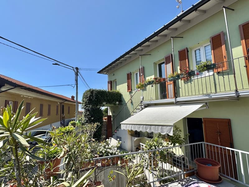 2-story residential building with green exterior walls, balconies, and potted plants on the balconies. The building has a slanted roof and there are power lines visible in the foreground.