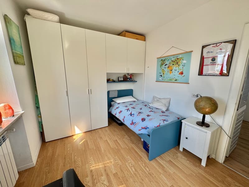 Bedroom with white wardrobe, blue bed frame, world map poster, wooden flooring, and a globe on a side table.