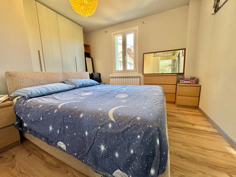 Spacious bedroom with hardwood flooring, a large bed with a starry night-themed comforter, a wardrobe, a dresser, and a decorative light fixture on the ceiling.