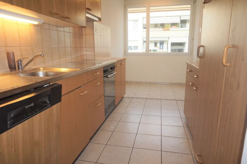 Stainless steel sink, dishwasher, oven, wooden cabinets, tiled floor, light over counter