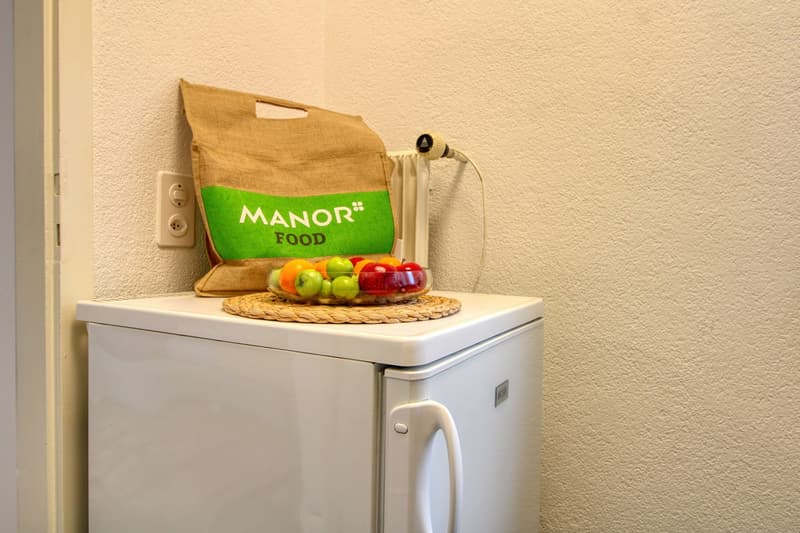 small white refrigerator, brown bag with 'Manor Food', bowl of fruit on top