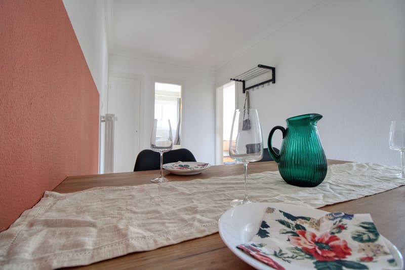 wooden table with wine glasses and tableware, walls are painted in red and white, a black coat rack is mounted on the wall