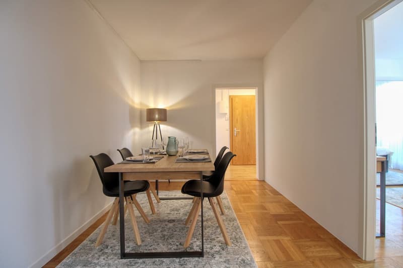 Dining room with wooden table, black chairs, lamp, rug, and wooden floor