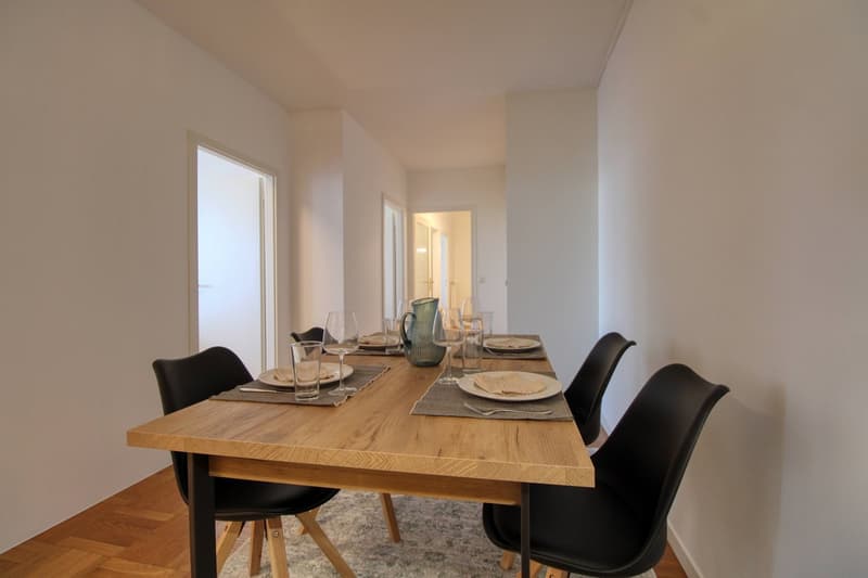 Dining room with a wooden table, black chairs, and a white wall