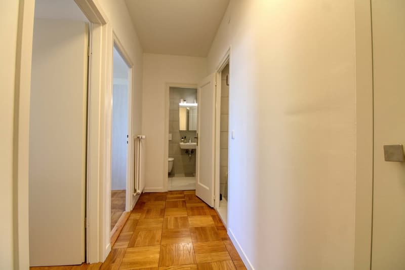 Empty hallway with wooden floor, white walls, and doors leading to different rooms.