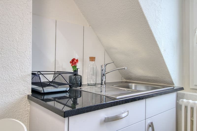 Small kitchen area, stainless steel sink, faucet, countertop, white cabinets, metal dish rack, vase with flower