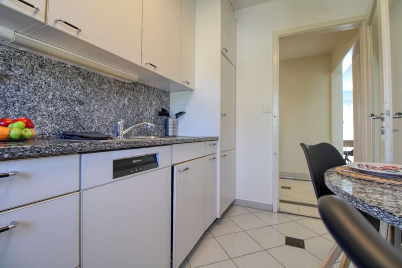 Granite countertop, white cabinets, built-in dishwasher, tiled floor, dining table