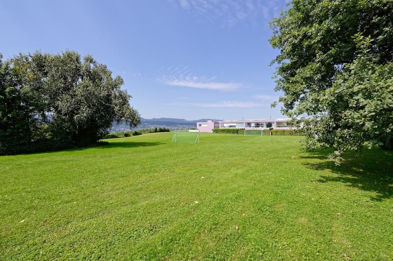 open field, goal post, large trees, building in the distance
