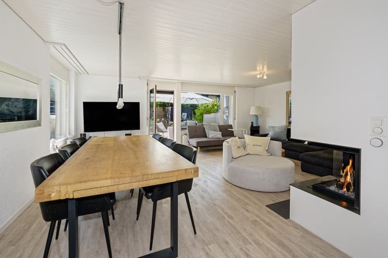 large open living area, dining table, sofa, armchair, fireplace, fire burning, windows