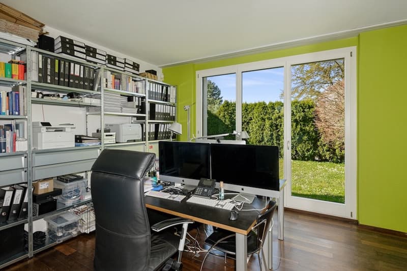 An office with a desk, black leather office chair, computer, large glass windows