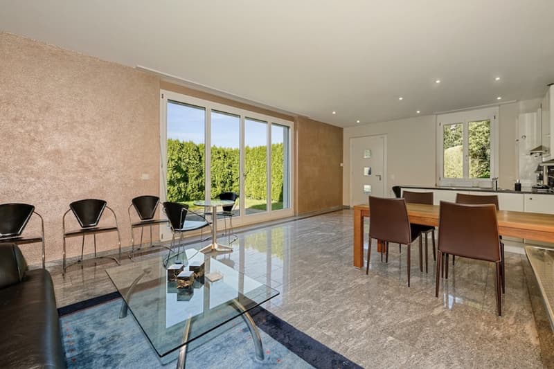 modern living room with large windows, glass table, chairs, couch, and a dining table