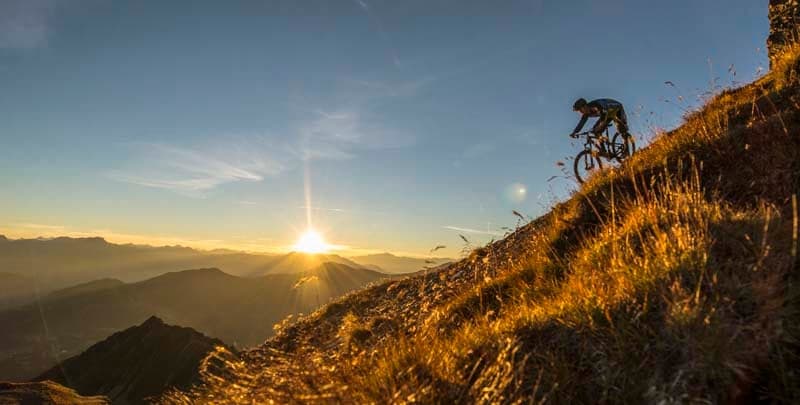 person riding a mountain bike on a mountain trail at sunset
