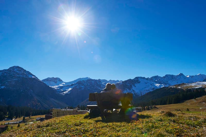 couple sitting on a bench, mountains in the background, sunny day
