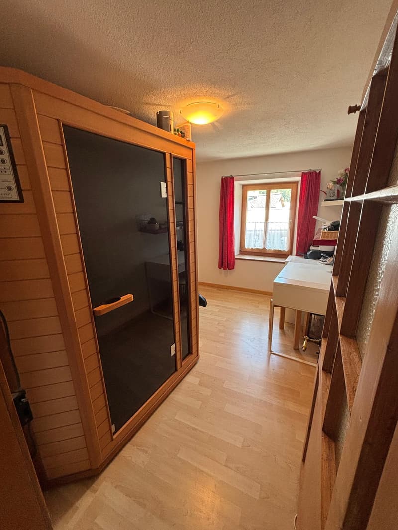 wooden sauna, desk, chair, window with red curtains, wooden floor, light, shelf with items, framed picture on wall