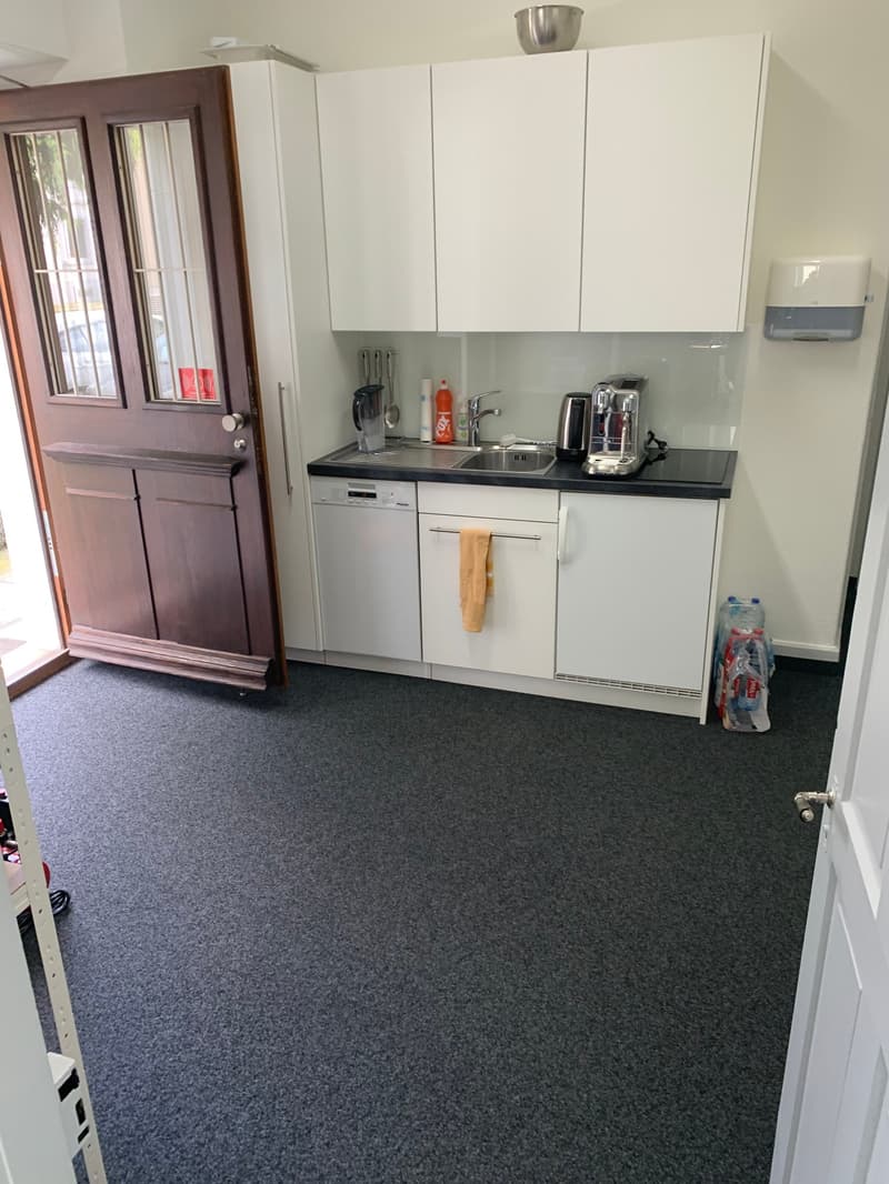 modern kitchen with white cabinets, black countertop, sink, dishwasher, coffee machine, towel, bottles, carpeted floor