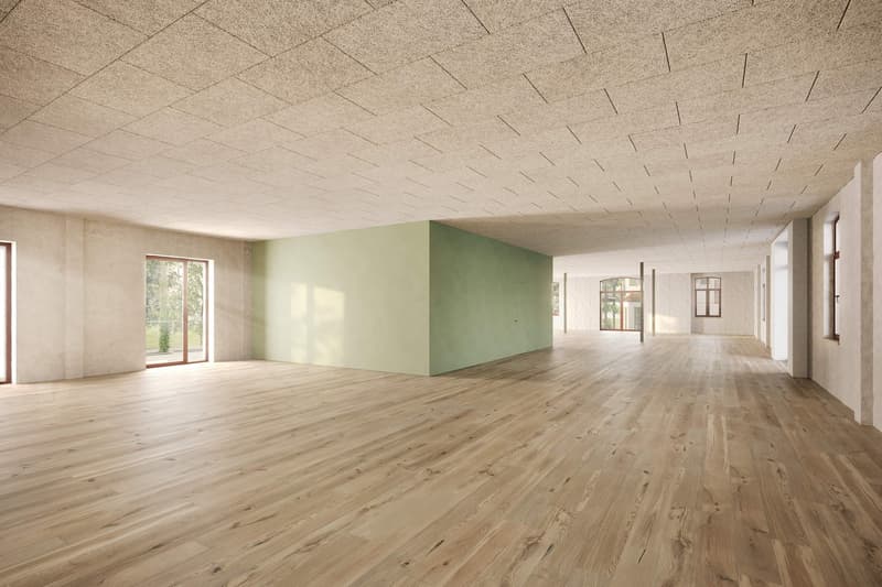 Large open space with wooden flooring, white walls, and a green accent wall. The room has large windows providing natural light. The ceiling has a textured pattern. The space appears to be a spacious, unfinished interior area.