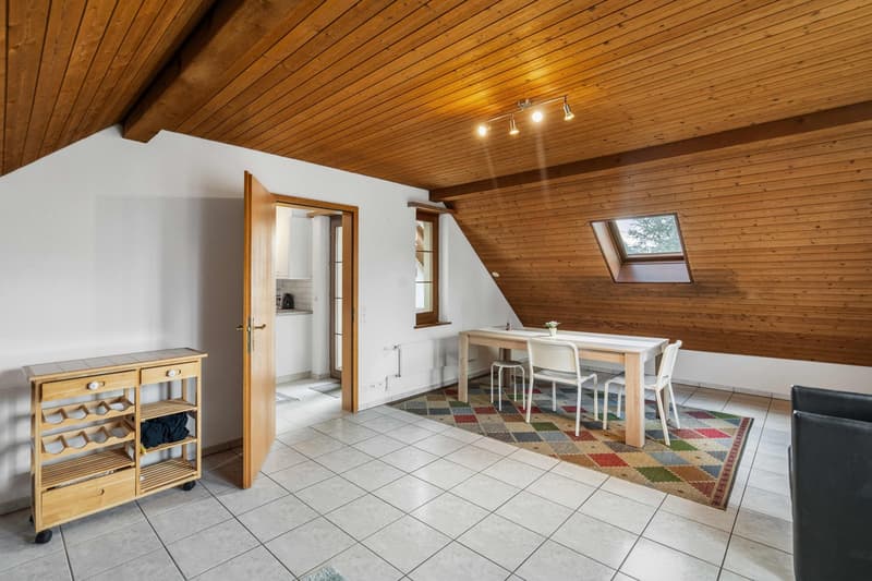 Dining room with wooden ceiling, white walls, table and chairs, wooden cart, black leather sofa.