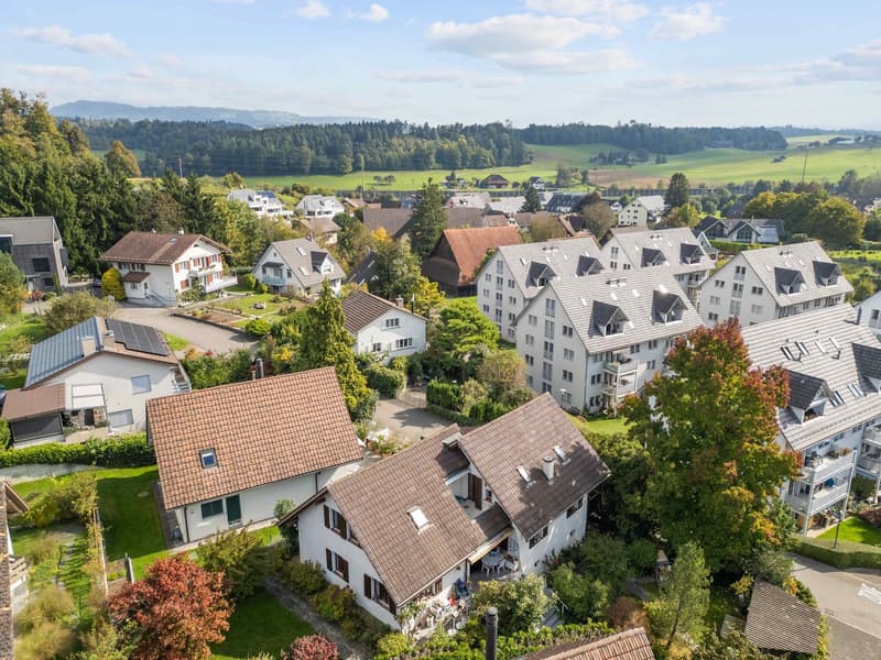 aerial view of neighborhood with residential houses of various sizes and styles, green surroundings, driveways, solar panels on some roofs