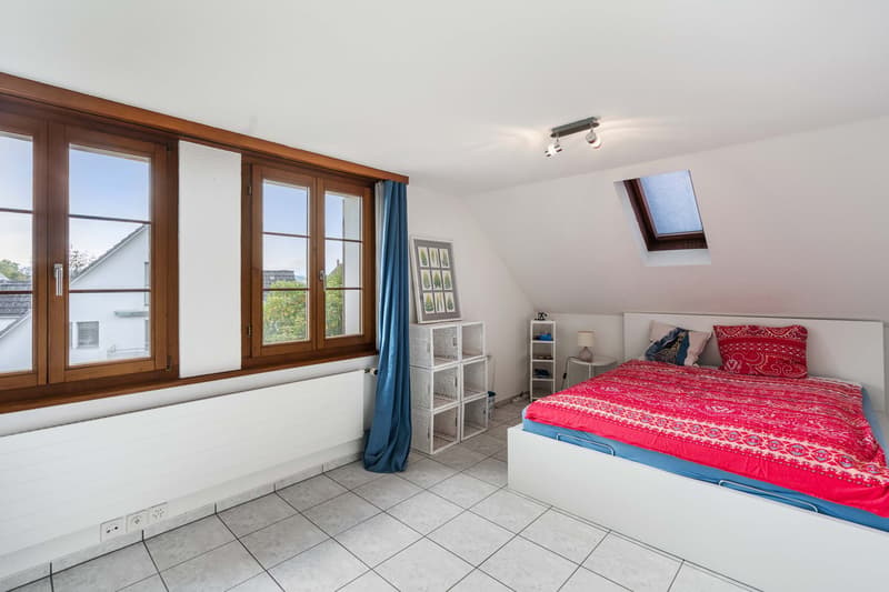 bedroom with large windows, bed with blue sheets and colorful blanket, skylight, storage baskets, radiator, white shelves, power outlets