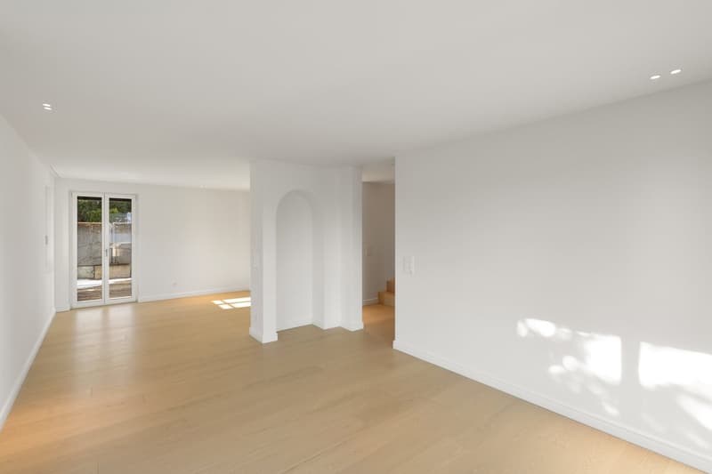 Empty room with wooden floors, white walls, sliding doors leading to a balcony, recessed lighting on the ceiling.