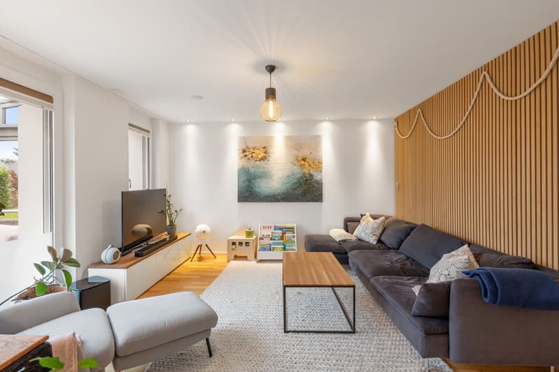 large gray sofa, wooden coffee table, large glass window, large screen television, white rug