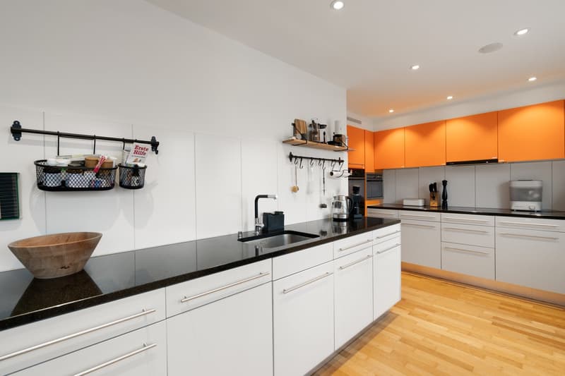 modern white kitchen with black countertops, white cabinets, dishwasher, wooden floor, hanging storage racks