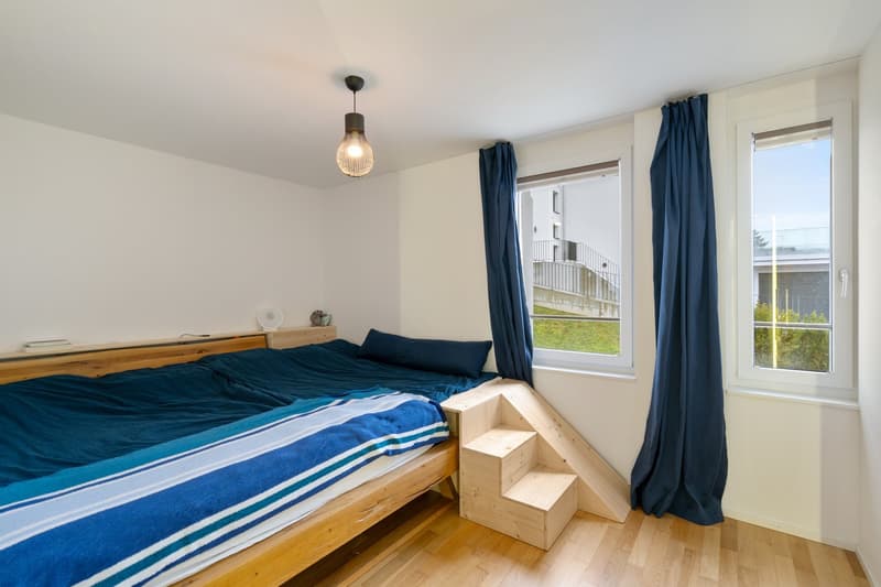 bedroom with wooden bed, wooden steps on the bed, bedside table, windows, lamp